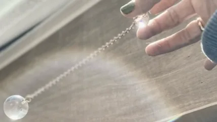a round ball pendulum held by fingers that have green nail polish