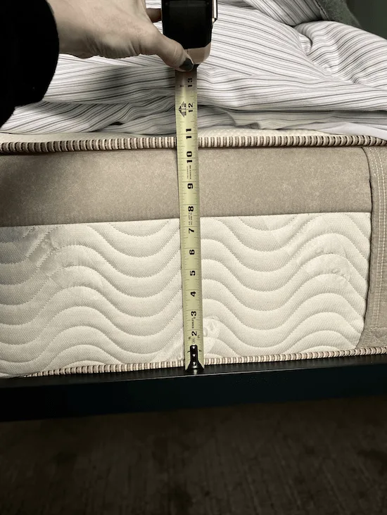 A measuring tape held up to the side of a mattress on a bed.