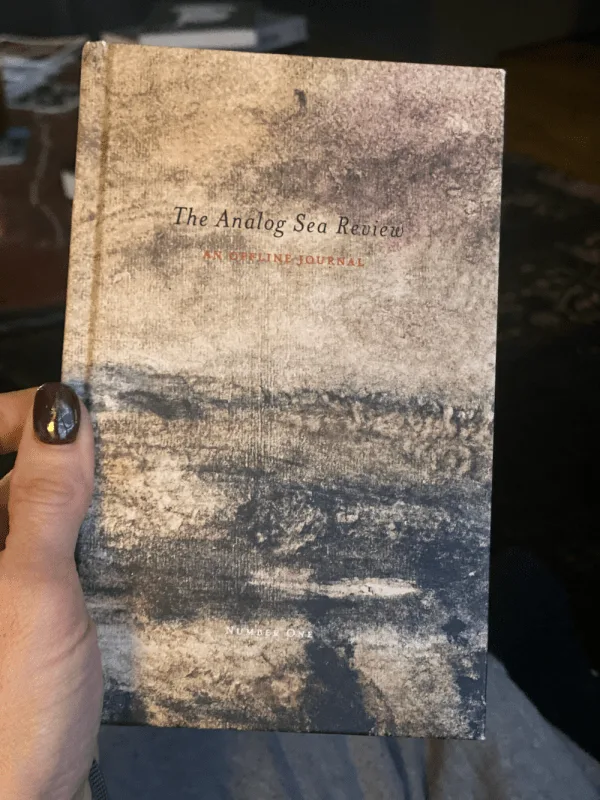 A photo of someone's hand holding a book that says on its cover, "The Analog Sea Review An Offline Journal Number One