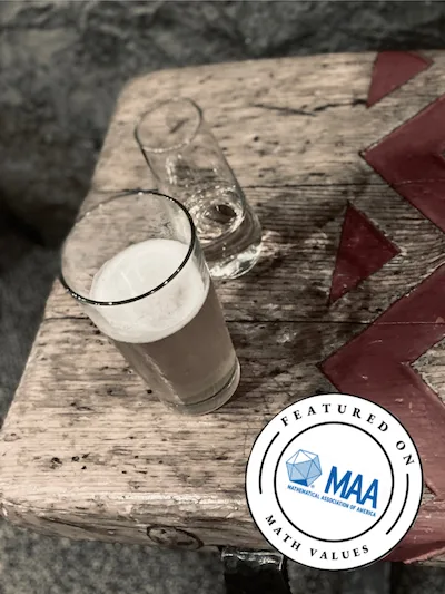 Photo of a glass of beer on a bench with a red herring bone pattern and a stamp on the photo that says this post has been featured on MAA site.