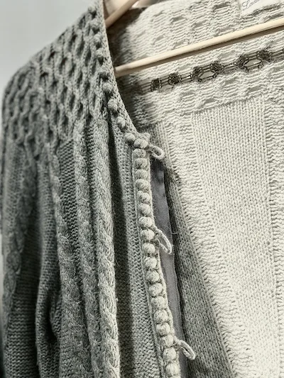 A cardigan on a hanger that has yarn loop closures.