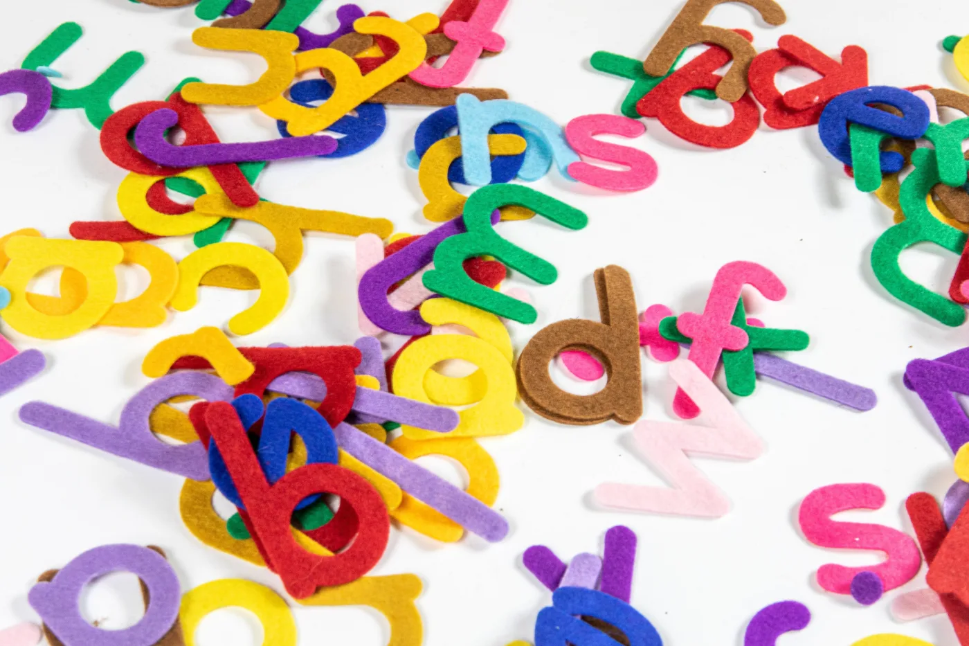 a scattered pile of colorful felt alphabet letters on top of a white surface