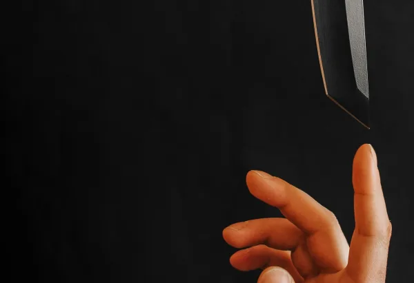 a hand in lower right with pointer finger upwards toward a knife blade that is coming from top towards finger