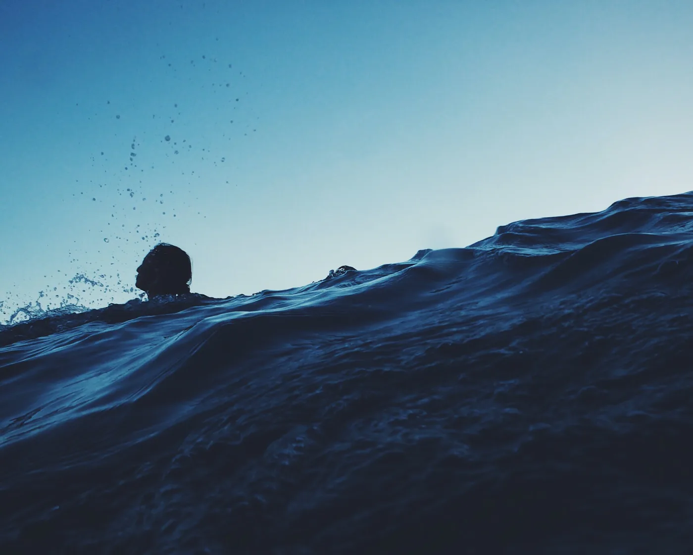 blue ocean water with a person's head, in shadow, above the top of a wave on the left side