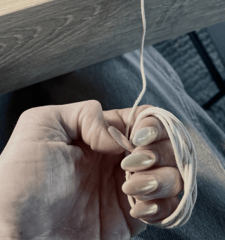 A hand with long fingernails holds a string that is wrapped around the fingers and extends upwards out of frame.
